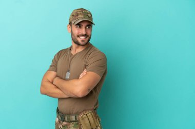 Mavi arka planda izole edilmiş, kolları bağlı ve mutlu bir ordu mensubu.