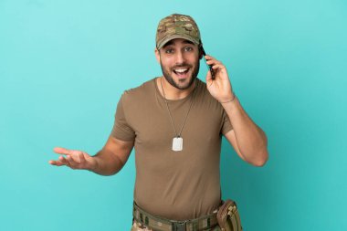 Mavi arka planda izole edilmiş künyeli ordu cep telefonuyla sohbet ediyor.