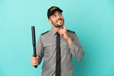 Genç güvenlik elemanı mavi arka planda izole edilmiş, araştırırken bir fikir düşünüyor.