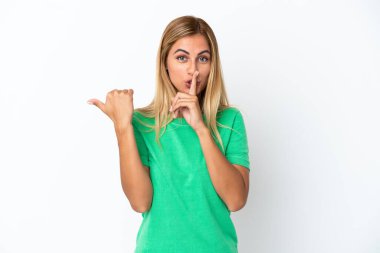 Sarışın Uruguaylı kız, beyaz arka planda izole edilmiş, kenarı işaret ediyor ve sessizlik hareketi yapıyor.