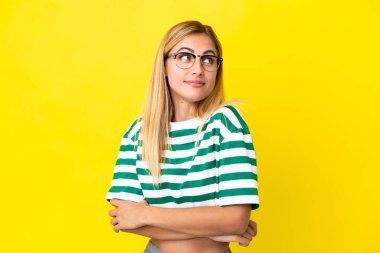 Sarışın Uruguaylı kız sarı arka planda izole edilmiş. Omuzlarını kaldırırken şüphe uyandıran hareketler yapıyor.