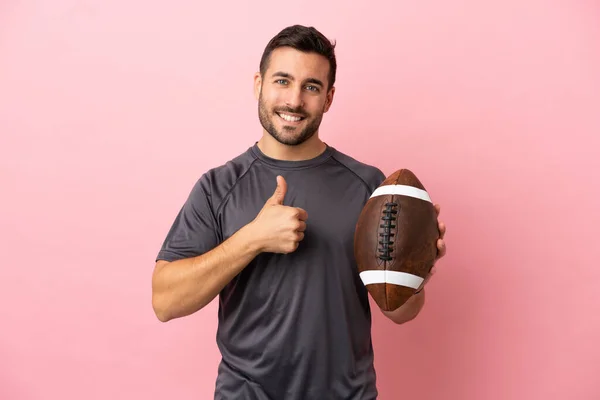 Young caucasian man playing rugby isolated on pink background giving a thumbs up gesture