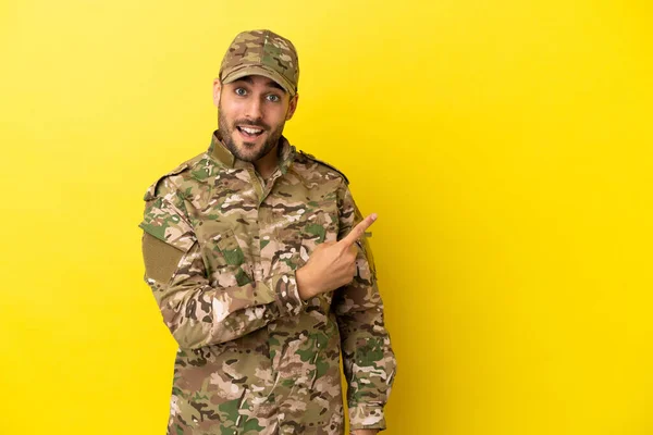 Military man isolated on yellow background pointing to the side to present a product