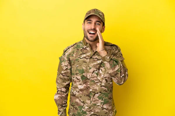 Military man isolated on yellow background shouting with mouth wide open