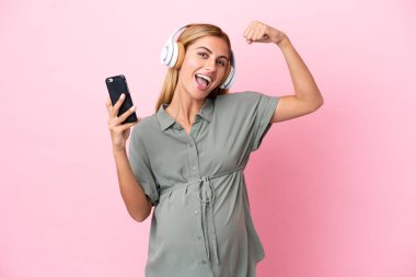 Genç Uruguaylı kadın mavi arka planda izole edilmiş hamile ve zaferi kutlarken müzik dinliyor.