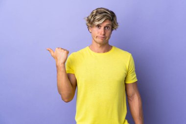 Münzevi mor arka planda mutsuz ve kenarı işaret eden İngiliz bir adam.