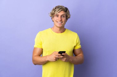 İzole edilmiş mor arkaplan üzerinde İngiliz adam cep telefonuyla bir mesaj gönderiyor