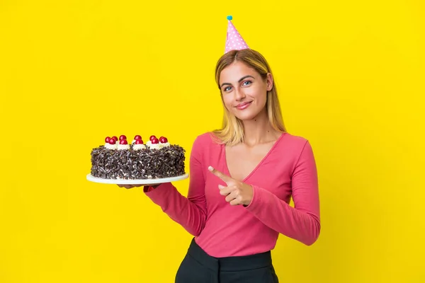Blondynka Urugwajska Dziewczyna Gospodarstwa Tort Urodzinowy Izolowane Żółtym Tle Wskazując — Zdjęcie stockowe