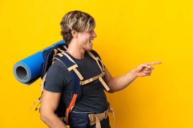 İzole edilmiş sarı arka planda genç dağcı parmak göstererek bir ürün sunuyor.