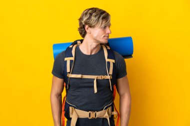 Genç dağcı yalıtılmış sarı arka planda yan tarafa bakıyor.