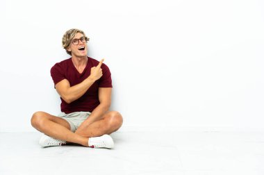 Yerde oturan genç İngiliz şaşırmış ve işaret ediyor.