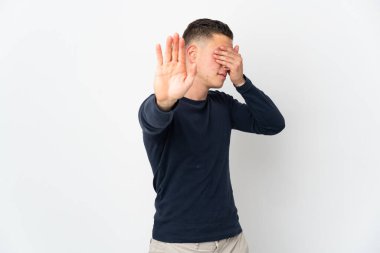 Beyaz arka planda izole edilmiş genç beyaz adam jesti durduruyor ve yüzünü kapatıyor.