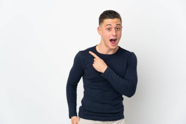 Beyaz arka planda izole edilmiş genç beyaz adam şaşırmış ve işaret ediyor.