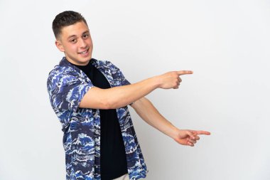 Beyaz arka planda izole edilmiş beyaz tenli genç adam parmağını yana doğru uzattı ve bir ürün sundu.