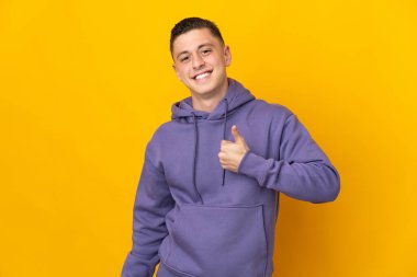 Sarı arka planda izole edilmiş genç beyaz bir adam baş parmak hareketi yapıyor.