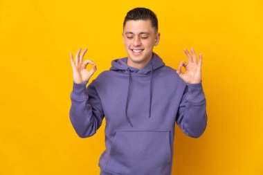 Zen pozisyonunda sarı arka planda izole edilmiş genç beyaz adam.