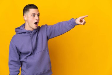 Young caucasian man isolated on yellow background pointing away