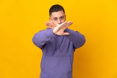 Sarı arka planda izole edilmiş genç beyaz bir adam bir eylemi durdurmak için eliyle jesti durduruyor.