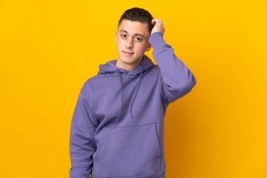 Kafkasyalı genç adam sarı arka planda izole edilmiş, hayal kırıklığı ifadesi var ve anlamıyor.