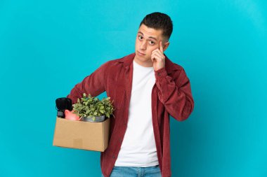 Young caucasian man making a move while picking up a box full of things isolated on blue background thinking an idea