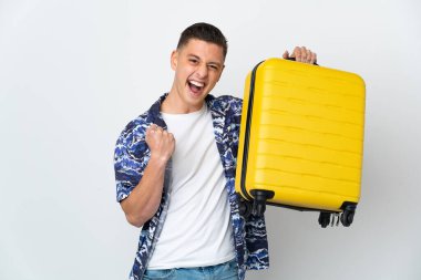 Beyaz arka planda izole edilmiş genç beyaz bir adam seyahat valiziyle geziyor.