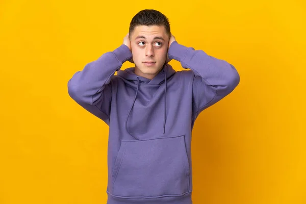 Young caucasian man isolated on yellow background frustrated and covering ears