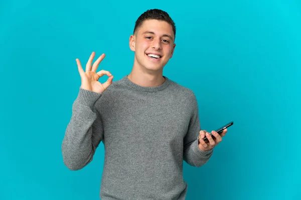Νεαρός Καυκάσιος Άνδρας Απομονωμένος Μπλε Φόντο Χρησιμοποιώντας Κινητό Τηλέφωνο Και — Φωτογραφία Αρχείου
