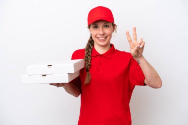 Pizza dağıtan kadın iş üniformalı beyaz arka planda izole edilmiş pizza kutuları alıyor gülümsüyor ve zafer işareti gösteriyor.