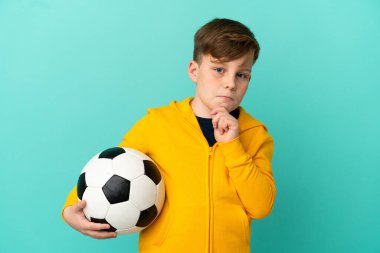 Mavi arka planda izole bir şekilde futbol oynayan kızıl saçlı çocuğun şüpheleri ve düşünceleri var.