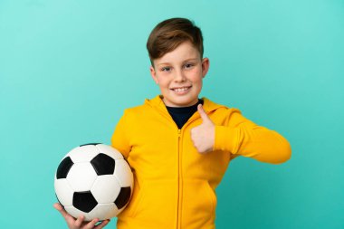 Kırmızı saçlı çocuk mavi arka planda izole bir şekilde futbol oynuyor.