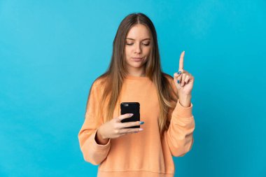 Genç Litvanyalı kadın mavi arka planda cep telefonu ve parmak kaldırarak izole edilmiş.