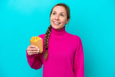 Kafkasyalı genç bir kadın elinde kızarmış cipslerle mavi arka planda izole edilmiş bir şekilde yukarı bakarken bir fikir düşünüyor.