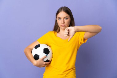 Genç Litvanyalı futbolcu kadın, mor arka planda izole edilmiş, olumsuz ifadeyle baş parmağını aşağı gösteriyor.