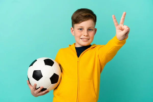 Roodharige Kind Spelen Voetbal Geïsoleerd Blauwe Achtergrond Glimlachen Tonen Overwinning — Stockfoto