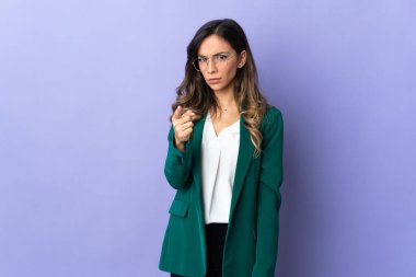 Mor arka planda izole edilmiş genç beyaz kadın hayal kırıklığına uğramış ve ön tarafı işaret ediyor.