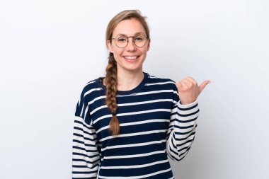 Beyaz arka planda izole edilmiş genç beyaz kadın bir ürünü sunmak için kenarı işaret ediyor.