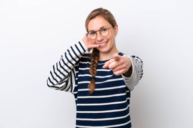 Beyaz arka planda izole edilmiş genç beyaz bir kadın telefon hareketi yapıyor ve ön tarafı işaret ediyor.