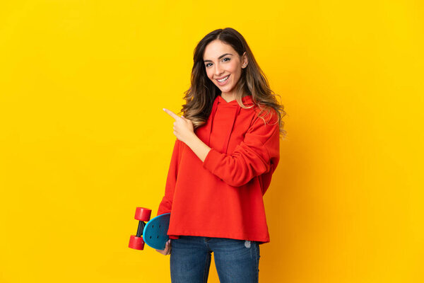 Young caucasian woman isolated on yellow background with a skate and pointing to the side