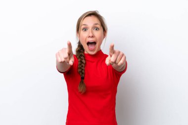 Beyaz arka planda izole edilmiş genç beyaz kadın şaşırmış ve ön tarafı işaret ediyor.