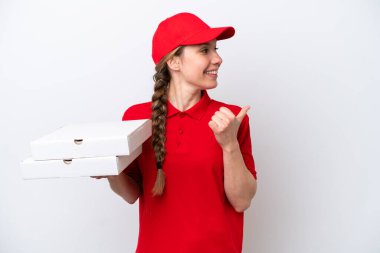 İş üniformalı bir pizzacı kadın beyaz arka planda izole edilmiş pizza kutularını topluyor ve bir ürün sunmak için yan tarafa bakıyor.