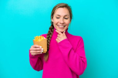 Genç beyaz kadın elinde kızarmış cipslerle mavi arka planda izole edilmiş bir şekilde yan tarafa bakıyor ve gülümsüyor.