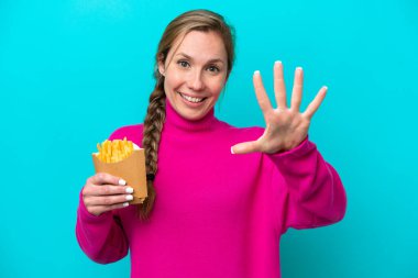 Mavi arka planda kızarmış cips tutan genç beyaz kadın parmaklarıyla beşi sayıyor.