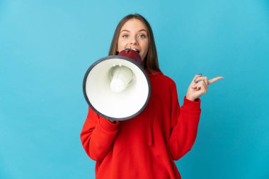 Young Lithuanian woman isolated on blue background shouting through a megaphone and pointing side