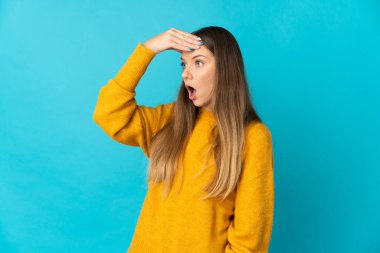 Mavi arka planda izole edilmiş genç Litvanyalı kadın yan tarafa bakarken sürpriz jest yapıyor.