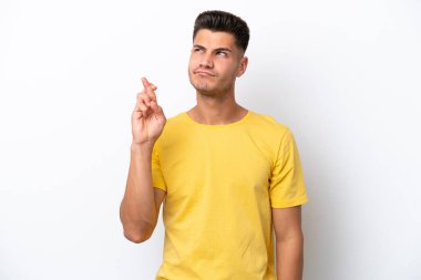 Beyaz arka planda izole olmuş genç beyaz bir adam parmaklarını çapraz yapıp en iyisini diliyor.