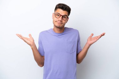 Beyaz arka planda izole olmuş genç beyaz bir adam şüphe içinde el kaldırırken