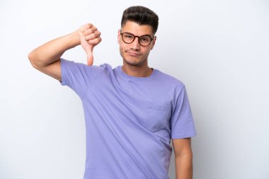 Beyaz arka planda izole genç beyaz adam olumsuz ifade ile baş parmağını göstermektedir