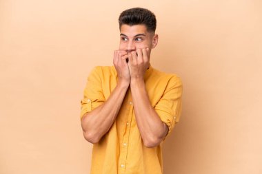 Beyazlı genç bir adam bej arka planda izole edilmiş gergin ve korkmuş bir şekilde elleriyle suni teneffüs yapıyor.