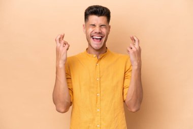 Beyazlı genç adam bej arka planda izole edilmiş ve şans diliyor.