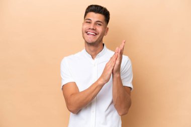 Beyazlı genç adam bej arka planda izole edilmiş bir konferansta sunumdan sonra alkışlıyor.